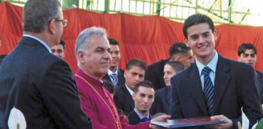 Bishop Suheil hands over a certificate and congratulates a graduate of St George's School Jerusalem