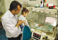 A father and his daughter check on their baby in the neonatal machine