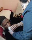 Helping a bedridden widow to drink a glass of milk