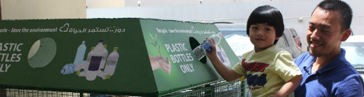 Little boy is lifted up to place bottle in recycling unit