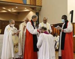Bishop Anthony Ball kneels in front of the communion table and the Archbishops