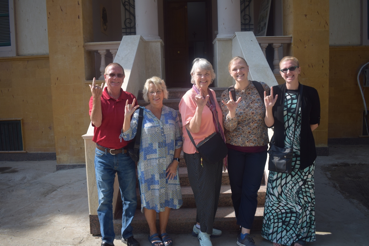 a group of American visitors make the sign for 'love' following a visit to the school