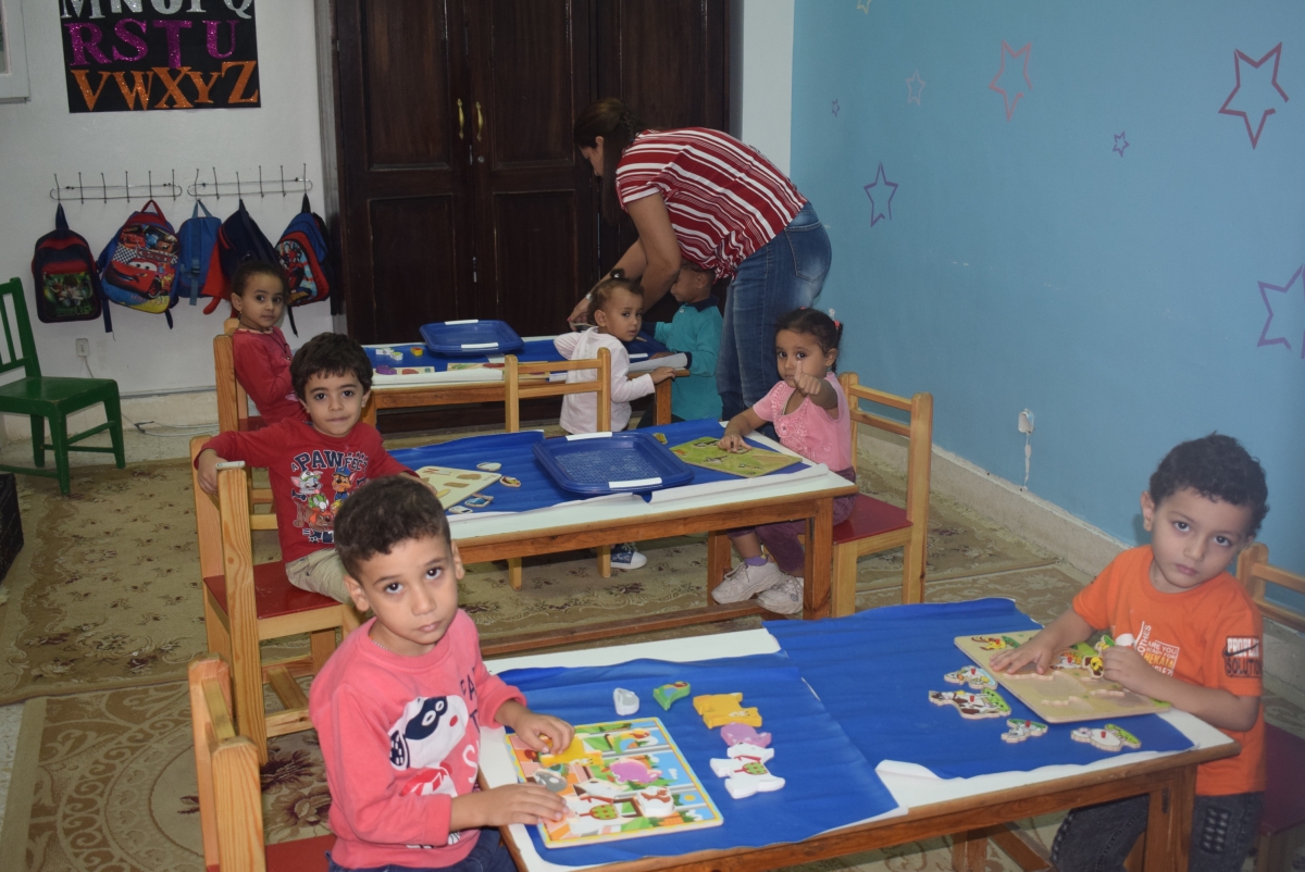 children sat at tables doing wooden jigsaws, at the pre-school