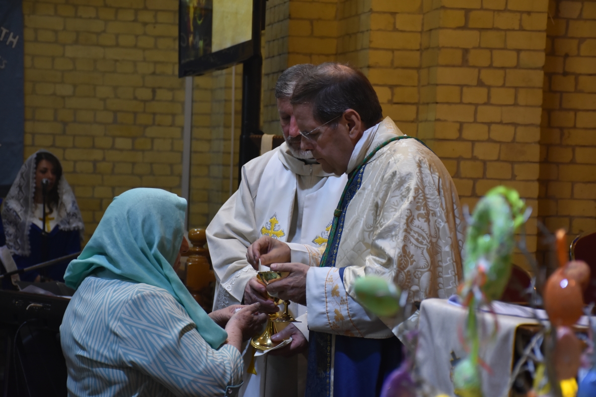 Archbishop Michael serving the eucharist to a lady with her head covered by a blue headscarf in St George's Church
