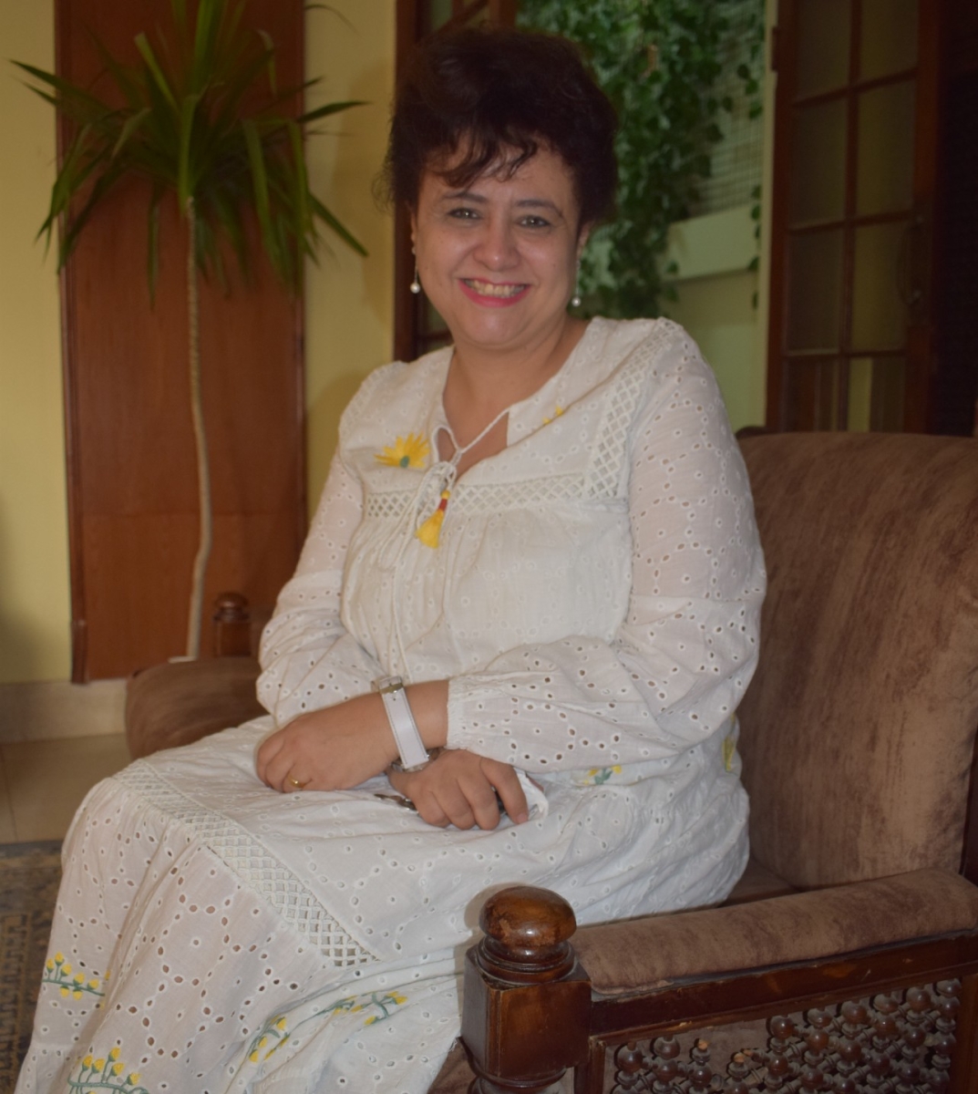 Dr Eman sat in a chair with her hands folded in her lap wearing a white dress