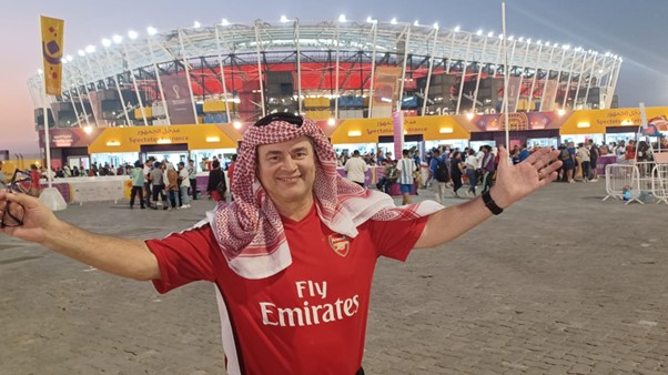 Father Mark in front of the stadium in a red Arsenal top and local headress