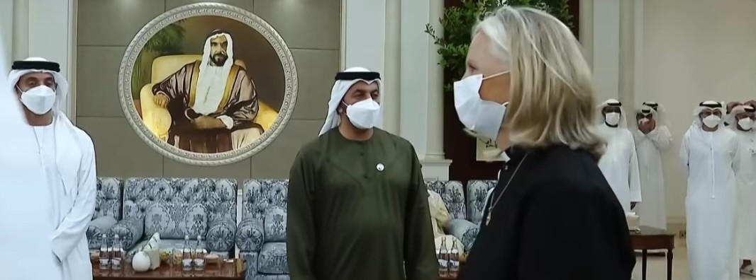 Mother Christine wearing traditional black priest clothing and a face mask walking through a stately room with arabs in traditional thobes and headware
