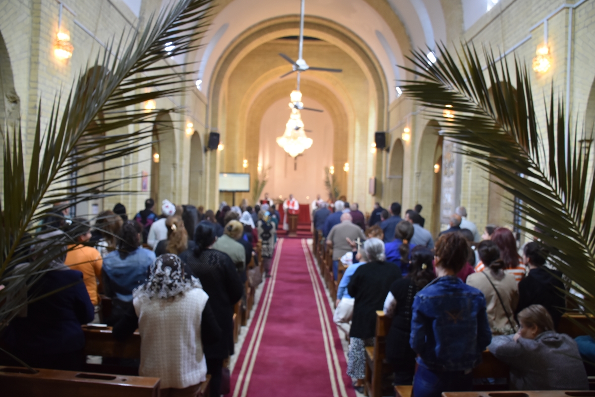 Looking up the aisle of the church between two large palm branches, the pews filled with people