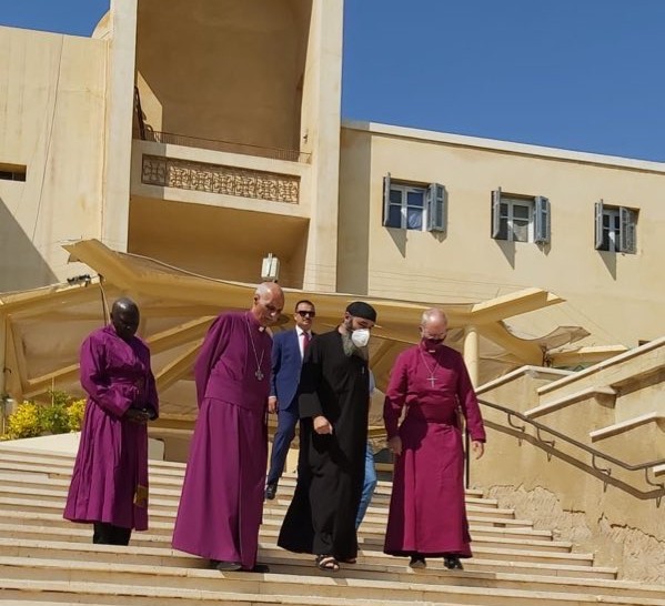 Justin Welby, Samy Fawzy, Anthony Poggo decend the front steps of the monastery with the head of the monastery wearing a protective face mask