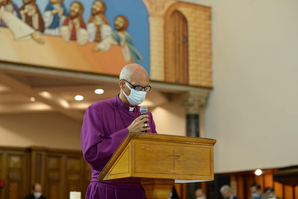 Bishop Samy giving his speech at the lectern in the cathedral wearing a face mask