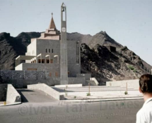 The All Saints Church white building and bell tower in front of the mountain when it first opened